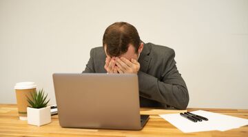 Een man die balend achter zijn laptop zit, misschien omdat hij het ongelukkigste beroep beoefent